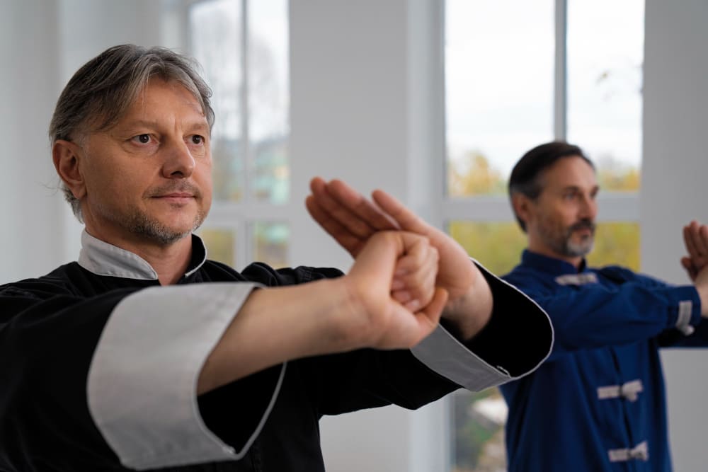hombre adulto practicando artes marciales en sala con otros alumnos en segundo plano