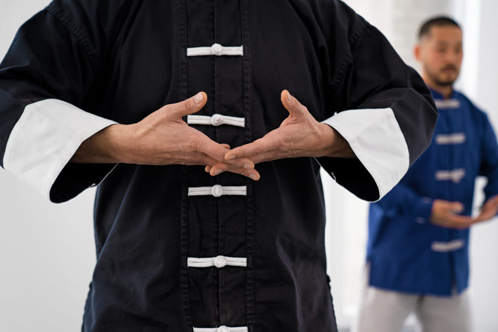 persona con uniforme negro de kung fu realizando posicion de manos en sala de entrenamiento